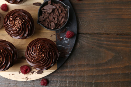 Tasty cupcakes with chocolate cream and raspberries on wooden table, flat lay. Space for textの写真素材