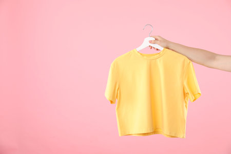 Woman holding hanger with yellow t-shirt on pink background, closeup. Space for textの写真素材
