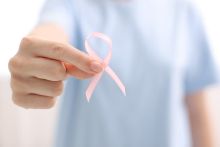 Woman with pink ribbon on light background, closeup. Breast cancer awarenessの写真素材