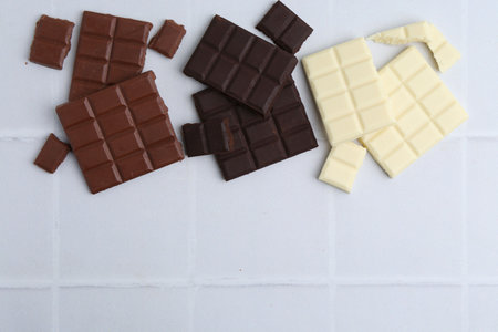 Different types of chocolate on white tiled table, flat lay. Space for text