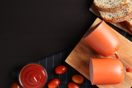 Tasty boiled sausage, ketchup, tomatoes and bread on black wooden table, top view. Space for textの写真素材
