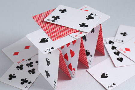 Collapsed house of playing cards on light gray background, closeup