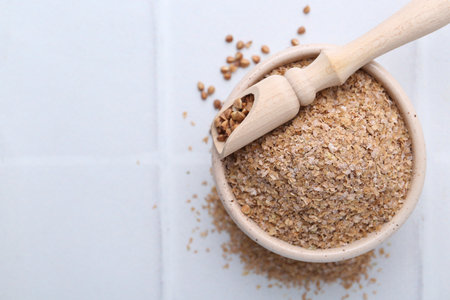 Buckwheat bran in bowl and grains on white table, top view. Space for textの写真素材