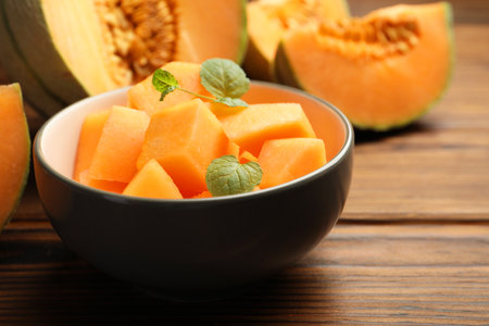 Pieces of Cantaloupe melon and mint in bowl on wooden table, closeupの写真素材