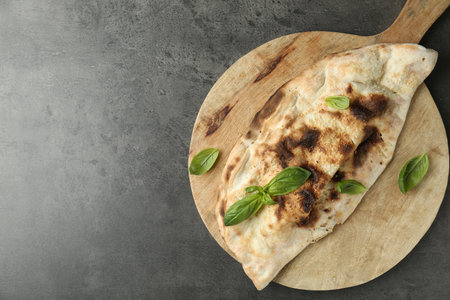 Delicious calzone with fresh basil on gray textured table, top view. Space for text
