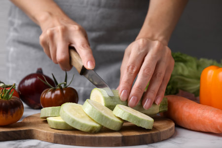Cooking vegetable stew. Woman cutting zucchini at white marble table, closeupの写真素材