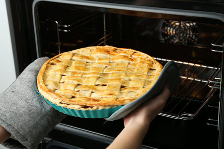 Woman taking delicious homemade apple pie out of oven in kitchen, closeupの写真素材