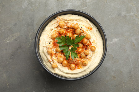 Delicious hummus with parsley, paprika and chickpeas in bowl on gray table, top view