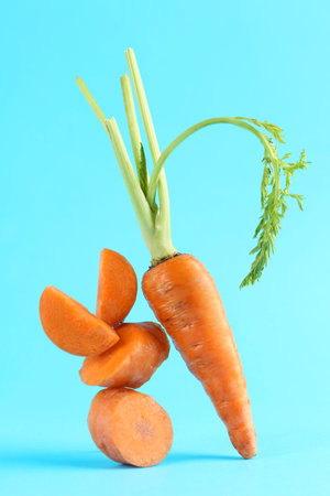 Whole and cut fresh carrots on light blue background