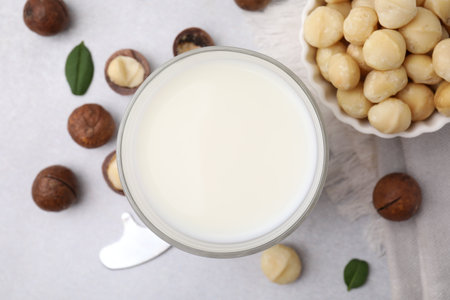 Glass of macadamia milk and nuts on white table, flat layの写真素材