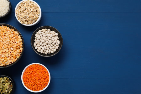 Different types of cereals, seeds and legumes on blue wooden table, flat lay. Space for text