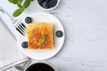 Slice of tasty semolina cake served on white textured table, flat lay. Space for text
