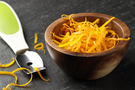Fresh orange zest and zester on black table, closeup
