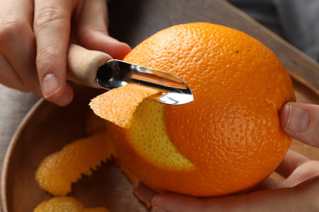 Woman zesting orange at wooden table, closeup