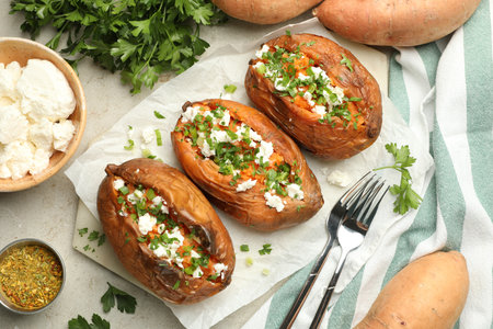 Tasty cooked sweet potatoes with feta cheese, green onion and parsley served on gray textured table, flat layの写真素材