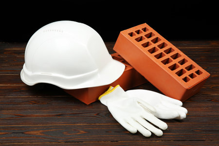 Red bricks, white hard hat and rubber gloves on wooden table. Building materialの写真素材