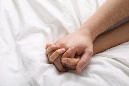 Lovely couple holding hands in bed, top view. Space for textの写真素材