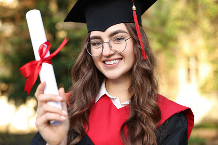Happy student with diploma after graduation ceremony outdoorsの写真素材
