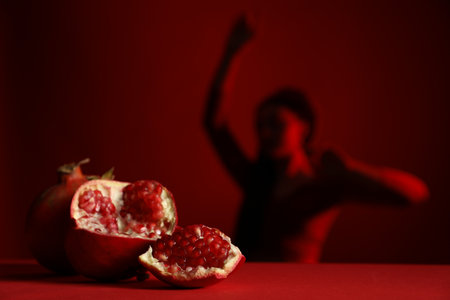 Woman posing against dark red background, focus on ripe pomegranateの写真素材