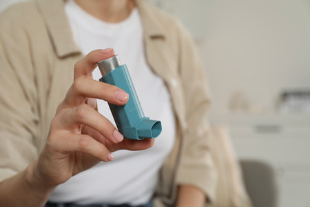 Woman holding asthma inhaler indoors, closeup. Space for textの写真素材