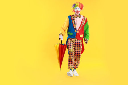 Happy clown with colorful umbrella on yellow backgroundの写真素材