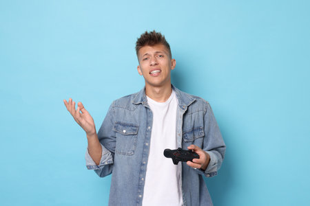 Unhappy young man with controller on light blue background