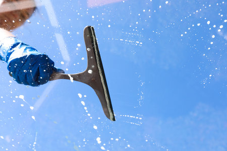Woman washing window with squeegee tool against blue sky, closeupの写真素材