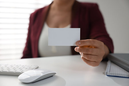 Woman holding blank business card at table in office, closeup. Mockup for designの写真素材