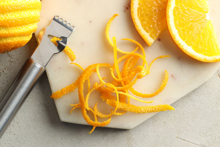 Fresh orange zest, slices of fruit and zester on light textured table, flat layの写真素材