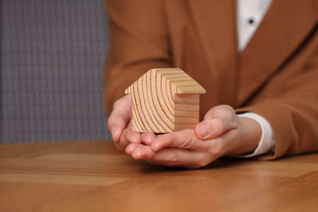 Property insurance. Real estate agent holding house figure at wooden table, closeupの写真素材