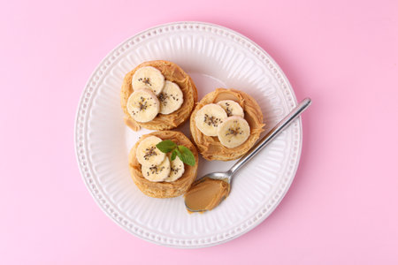 Tasty sandwiches with peanut butter, banana, chia seeds, mint and spoon on pink background, top viewの写真素材
