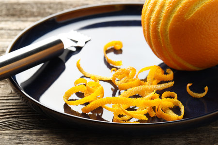 Fresh orange zest, fruit and zester on wooden table, closeupの写真素材