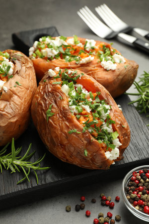 Tasty cooked sweet potatoes with feta cheese, green onion, parsley and spices on gray textured table, closeupの写真素材