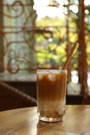 Glass of refreshing iced coffee and straw on wooden table outdoorsの写真素材
