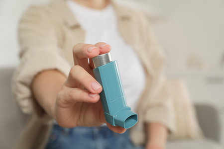 Woman holding asthma inhaler indoors, closeup. Space for textの写真素材