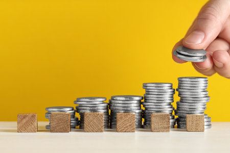 Woman putting coins and cubes with word Salary at white table against yellow background, closeup....