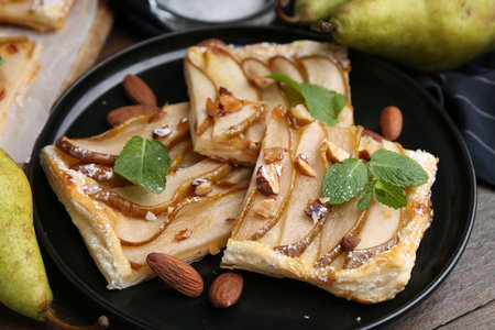 Pieces of tasty puff pastry pie with pears, mint and almonds on wooden table, closeupの写真素材