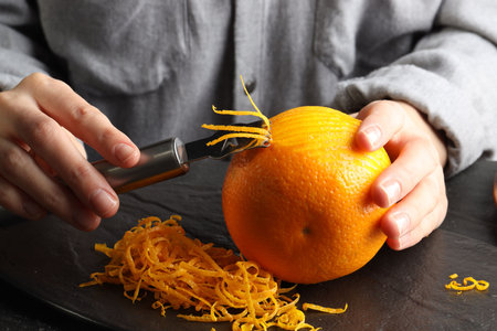 Woman zesting orange at black table, closeupの写真素材