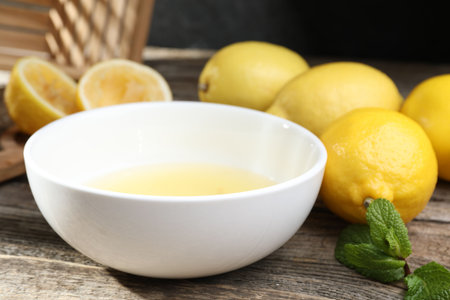 Fresh lemon juice in bowl and fruits on wooden table, closeupの写真素材