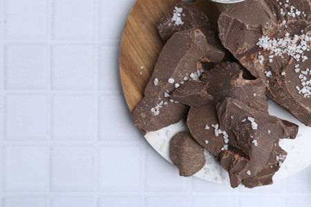 Pieces of tasty chocolate with salt on white tiled table, flat lay. Space for textの写真素材