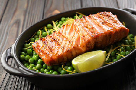 Delicious grilled salmon fillet with green peas and lime in baking dish on wooden table, closeupの写真素材
