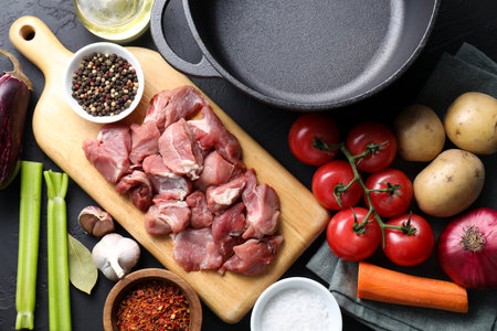 Cooking stew. Uncooked meat, vegetables and pot on black table, flat layの写真素材