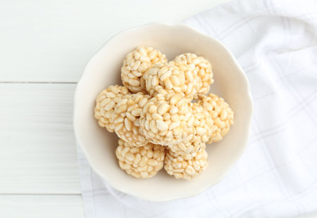 Tasty puffed rice balls in bowl on white wooden table, top viewの写真素材