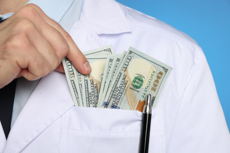 Corruption concept. Doctor putting dollar banknotes into his pocket on blue background, closeupの写真素材