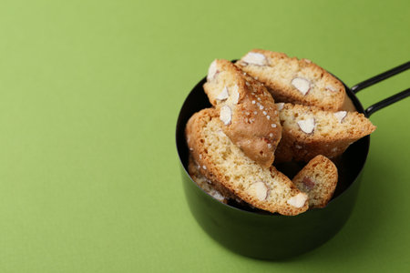 Tasty almond biscuits (Cantuccini) in scoop on green background, closeup. Space for textの写真素材