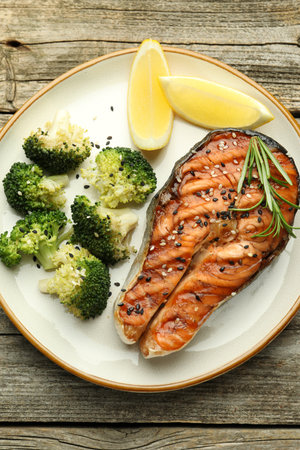 Tasty grilled salmon steak, broccoli, lemon and rosemary on wooden table, top viewの写真素材