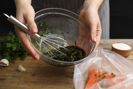 Woman with soy marinade and salmon fillet in plastic bag at wooden table, closeupの写真素材