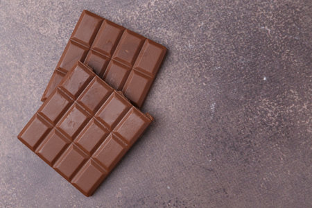 Pieces of delicious milk chocolate on brown table, top view. Space for text