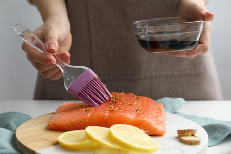 Woman marinating salmon fillet in dish at table, closeupの写真素材
