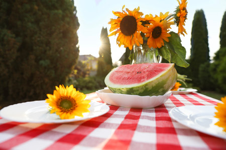 Vase of sunflowers, watermelon and plates on table in garden, closeupの写真素材